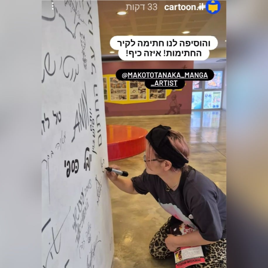 תמונה של יוצרת המנגה מאקוטו טאנאקה חותמת על קיר חתימות היוצרים במוזיאון